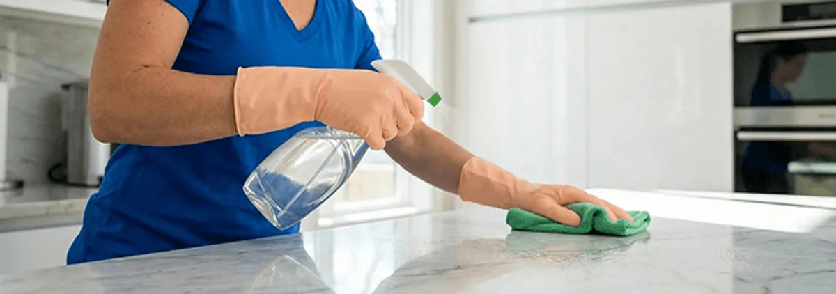 Maid service worker spraying and wiping a kitchen countertop with a microfiber cloth for sanitizing, Arlington, TX.
